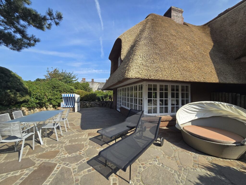 Terrasse mit Liegestühlen, einem Strandkorb und Gartenmöbeln vor einem Reetdachhaus