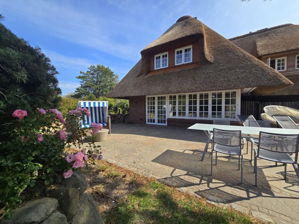 Terrasse eines Reetdachhauses mit Gartenmöbeln und Strandkorb.