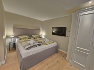Schlafzimmer mit grauem Doppelbett, TV und Holzboden.