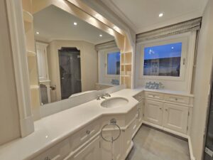Großes Badezimmer mit breitem Spiegel, weißem Waschbecken und separater Dusche.
