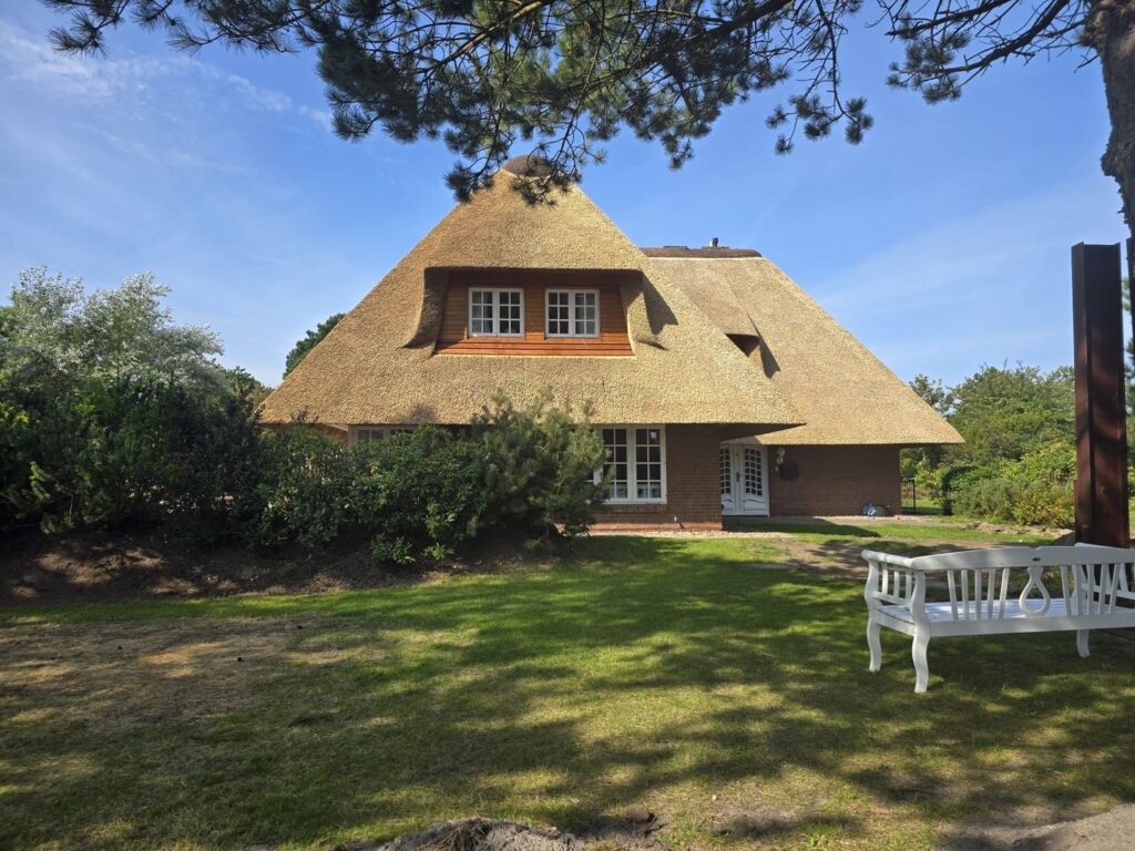 Reetdachhaus mit großem Garten und weißer Bank im Vordergrund.