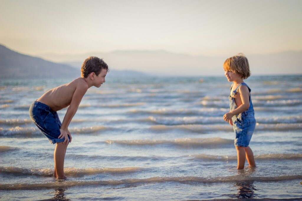 Zwei Kinder spielen im flachen Wasser am Strand bei Sonnenuntergang.